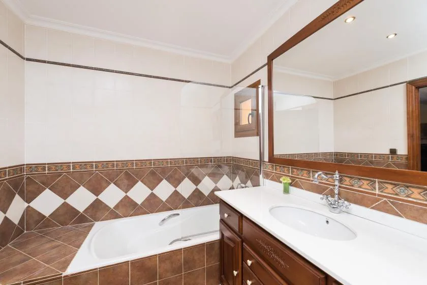 A tiled bathroom with a bathtub and a sink beneath a large mirror.