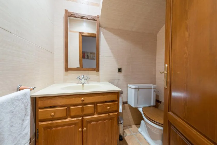 A tiled bathroom with a wooden vanity, mirror, and toilet.