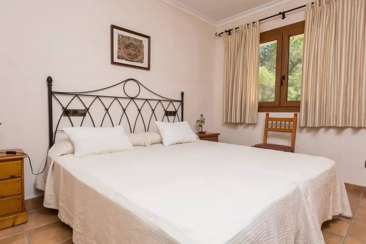 A bedroom with a large bed, framed artwork, and a window with curtains.
