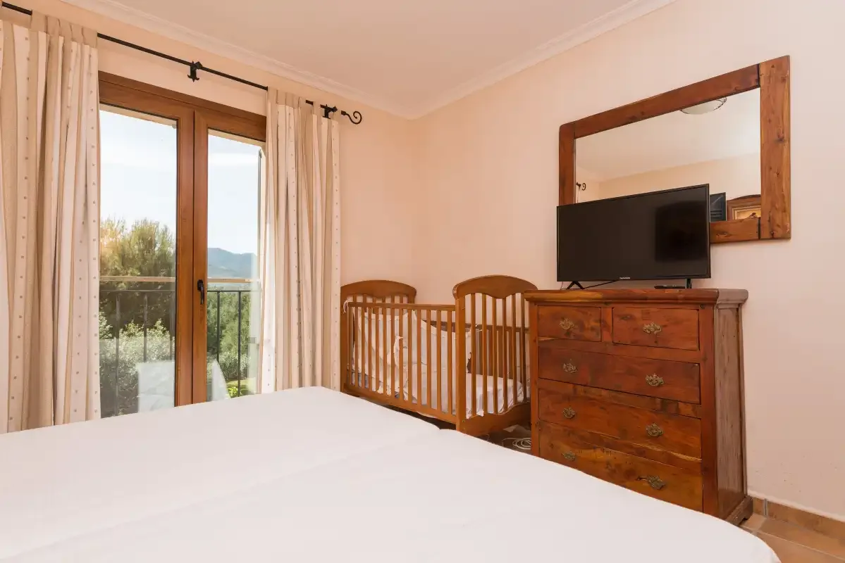 A bedroom with a bed, wooden cribs, and a dresser beneath a mirror.