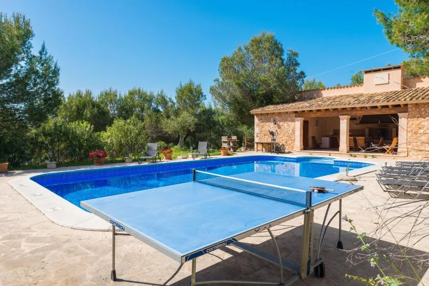 A swimming pool and outdoor table tennis table sit beside a stone house.