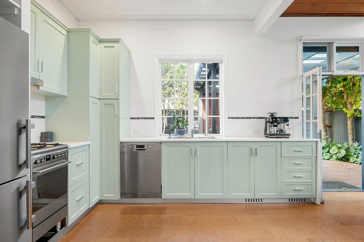 Una cocina verde menta con muebles claros, un horno de acero inoxidable y una ventana central.