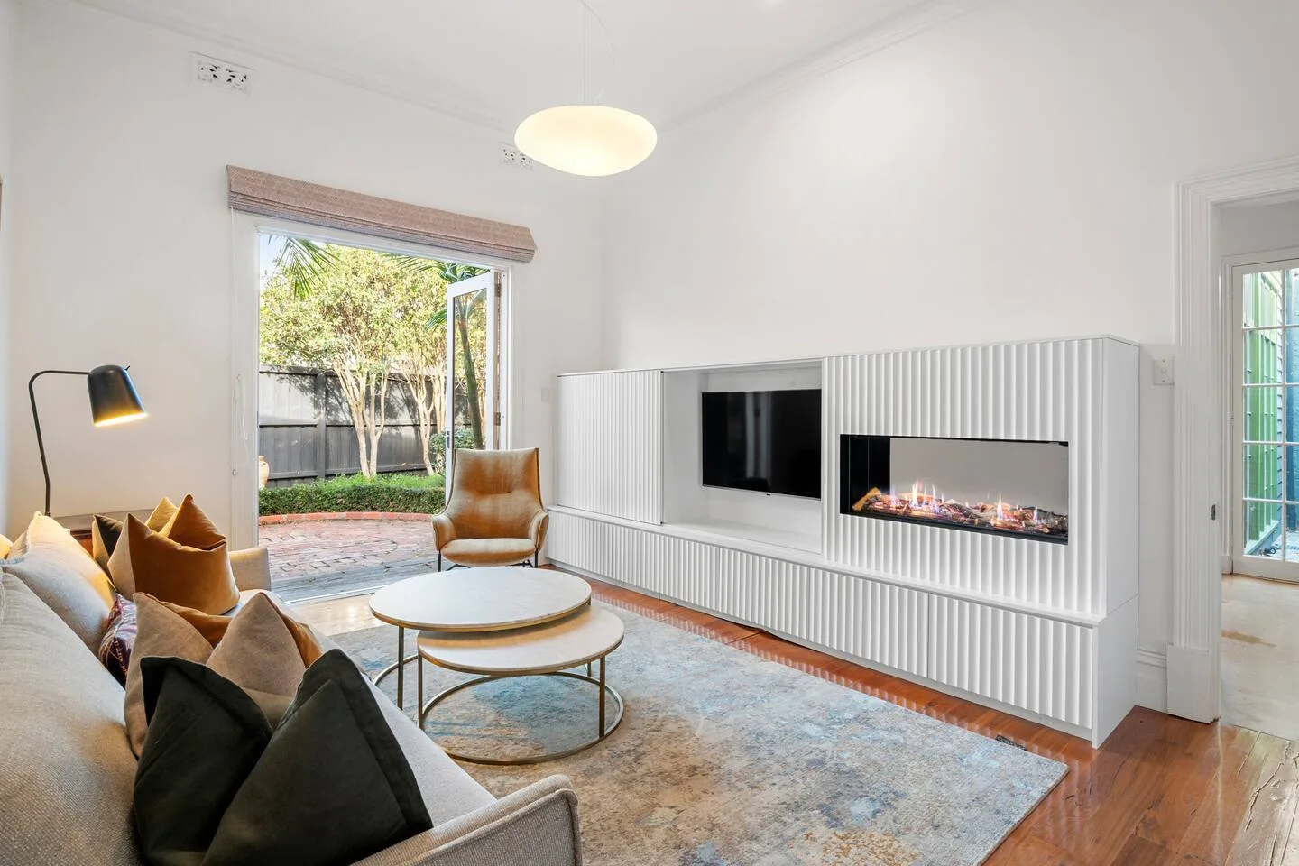 Una sala de estar luminosa con asientos y una chimenea empotrada junto a puertas de vidrio.