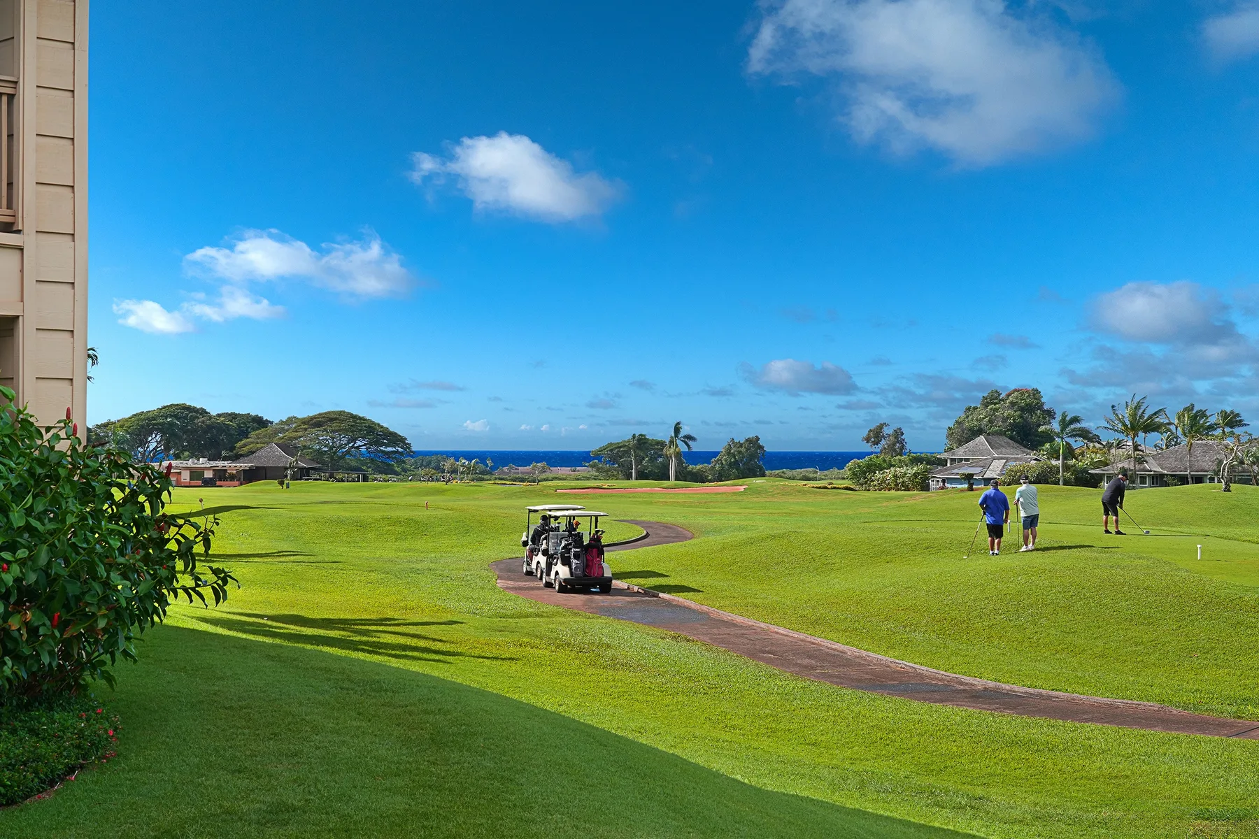 Un amplio campo de golf verde se extiende hacia el océano bajo un cielo azul.