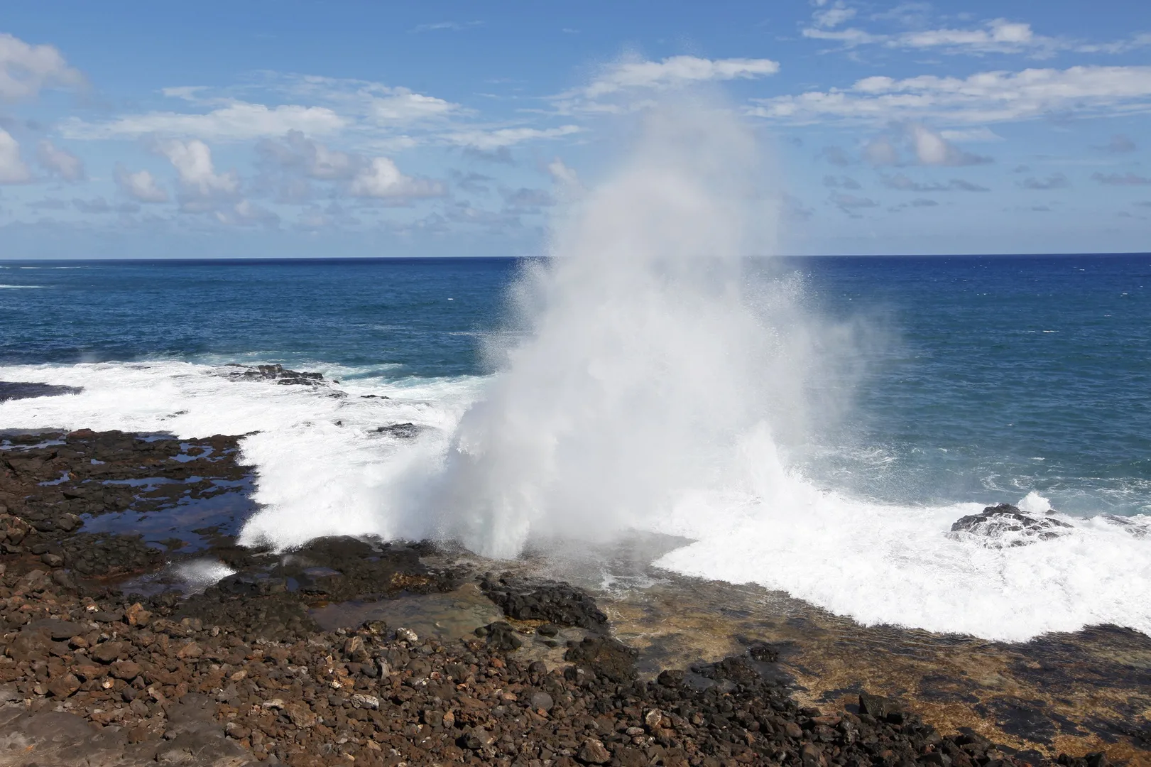 Las olas rompen contra una costa rocosa y levantan una columna de agua pulverizada.