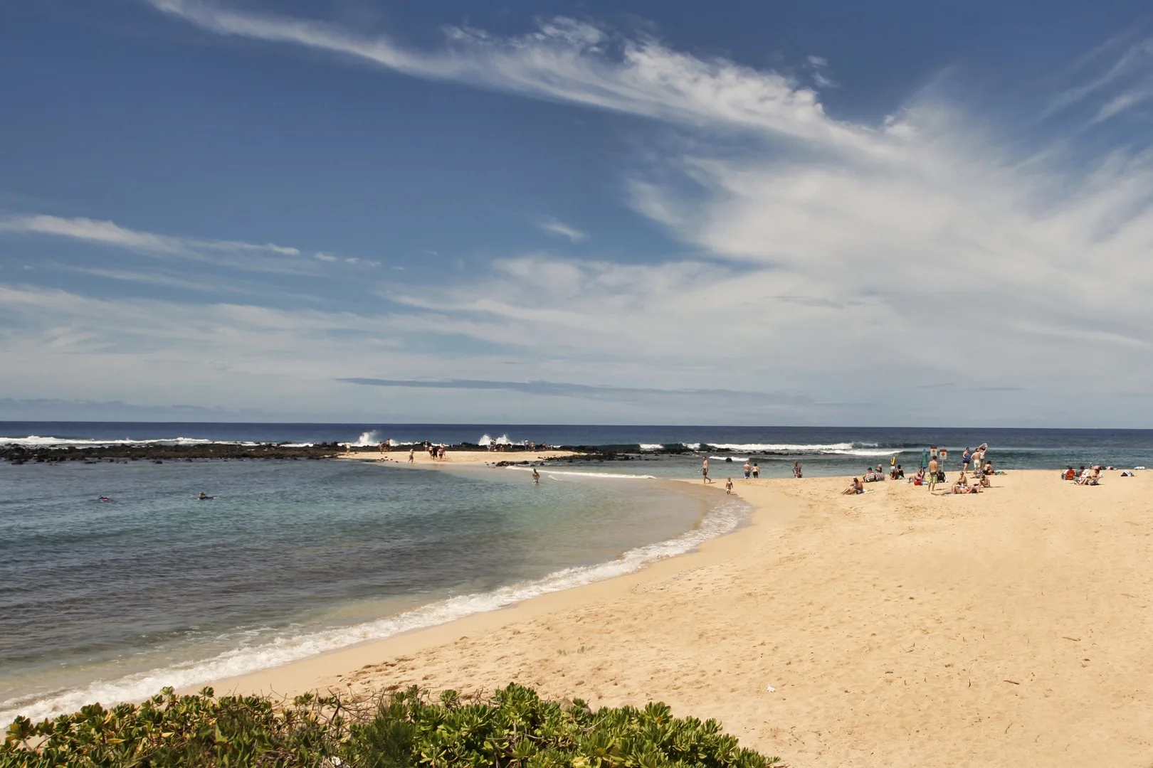 Una playa de arena rodea una ensenada poco profunda bajo un cielo parcialmente nublado.