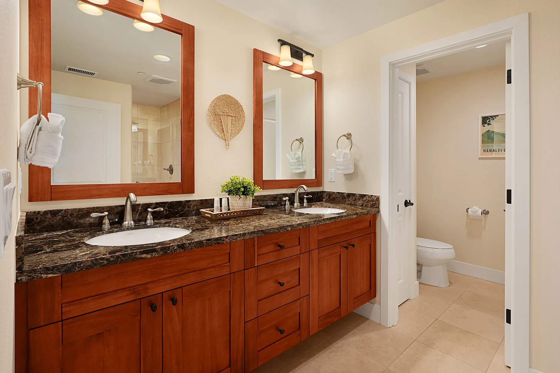 Un baño con un mueble largo de madera, lavabos sobre la encimera y una puerta al área del inodoro.