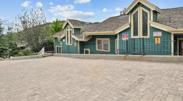 A green-trimmed building stands beside a broad paved courtyard with hills in the background.