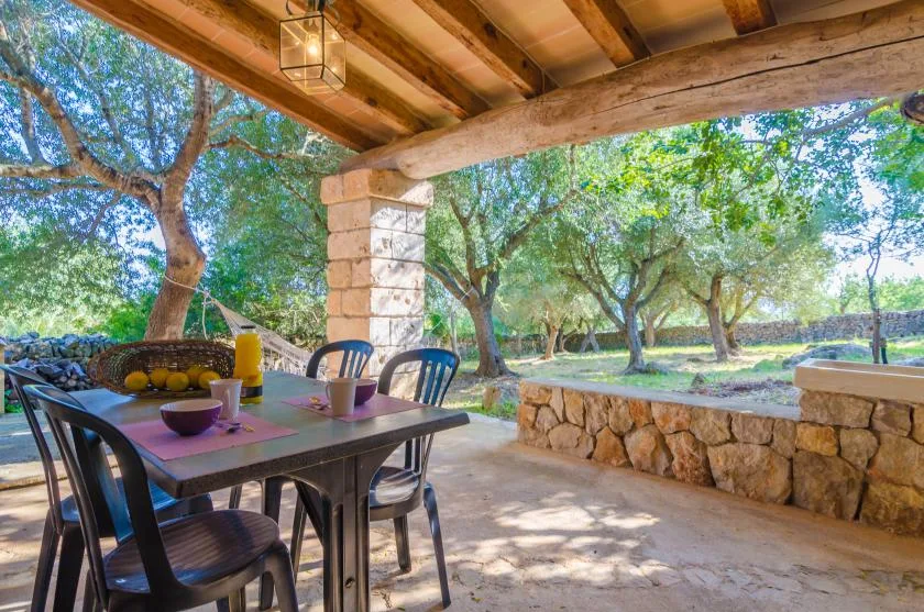 A covered outdoor dining area with a table overlooking a tree-filled garden.