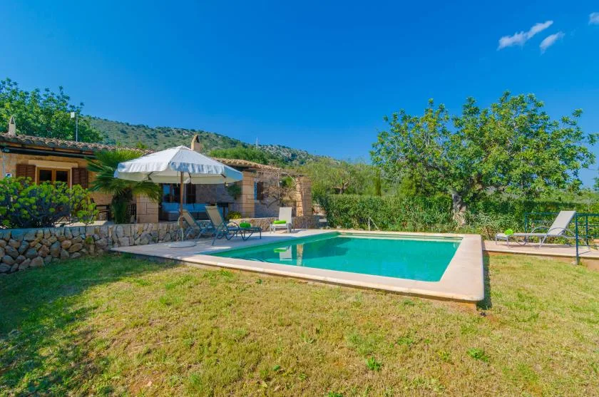 An outdoor swimming pool sits beside a landscaped garden and low stone wall.