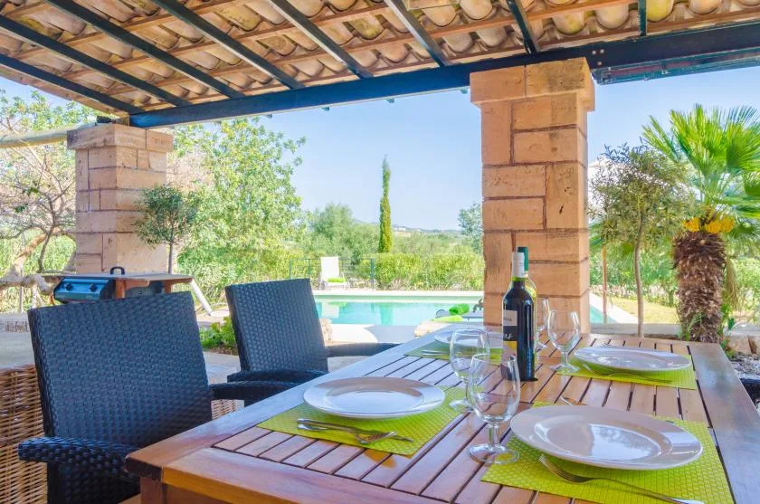 A covered outdoor dining area with a set table overlooking a swimming pool.