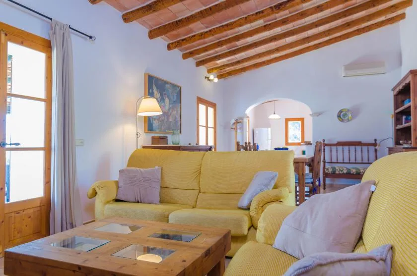 A living room with yellow seating, a wooden coffee table, and exposed ceiling beams.