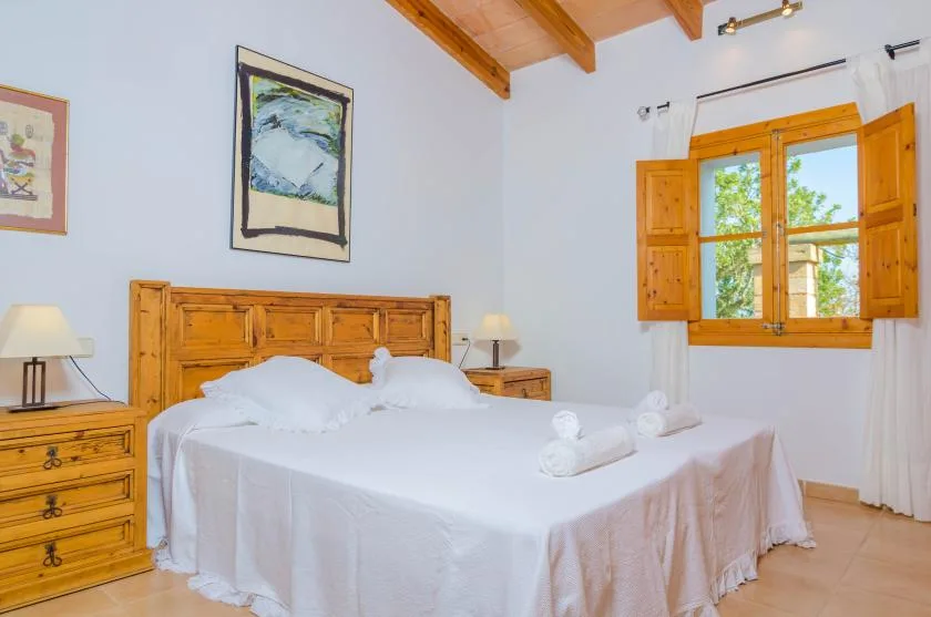 A bedroom with a wooden bed, white bedding, and a sunlit window.