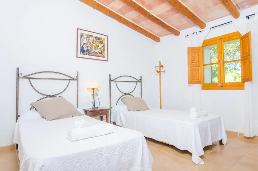 A bright bedroom with two single beds and a wooden-framed window.