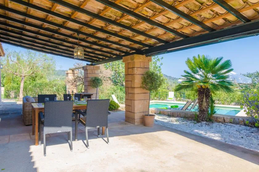 A covered patio with outdoor seating overlooks a swimming pool and palm tree.