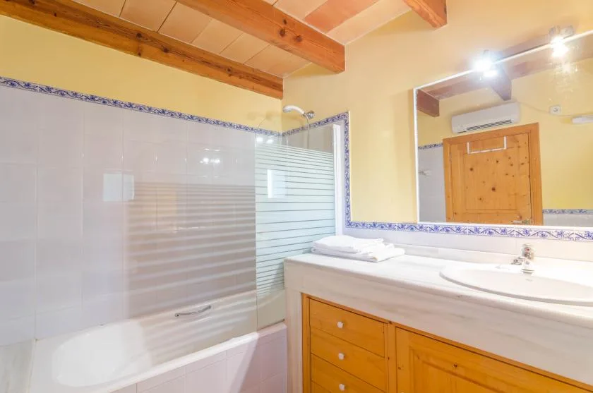 A bathroom with a bathtub, glass shower screen, and wooden vanity.