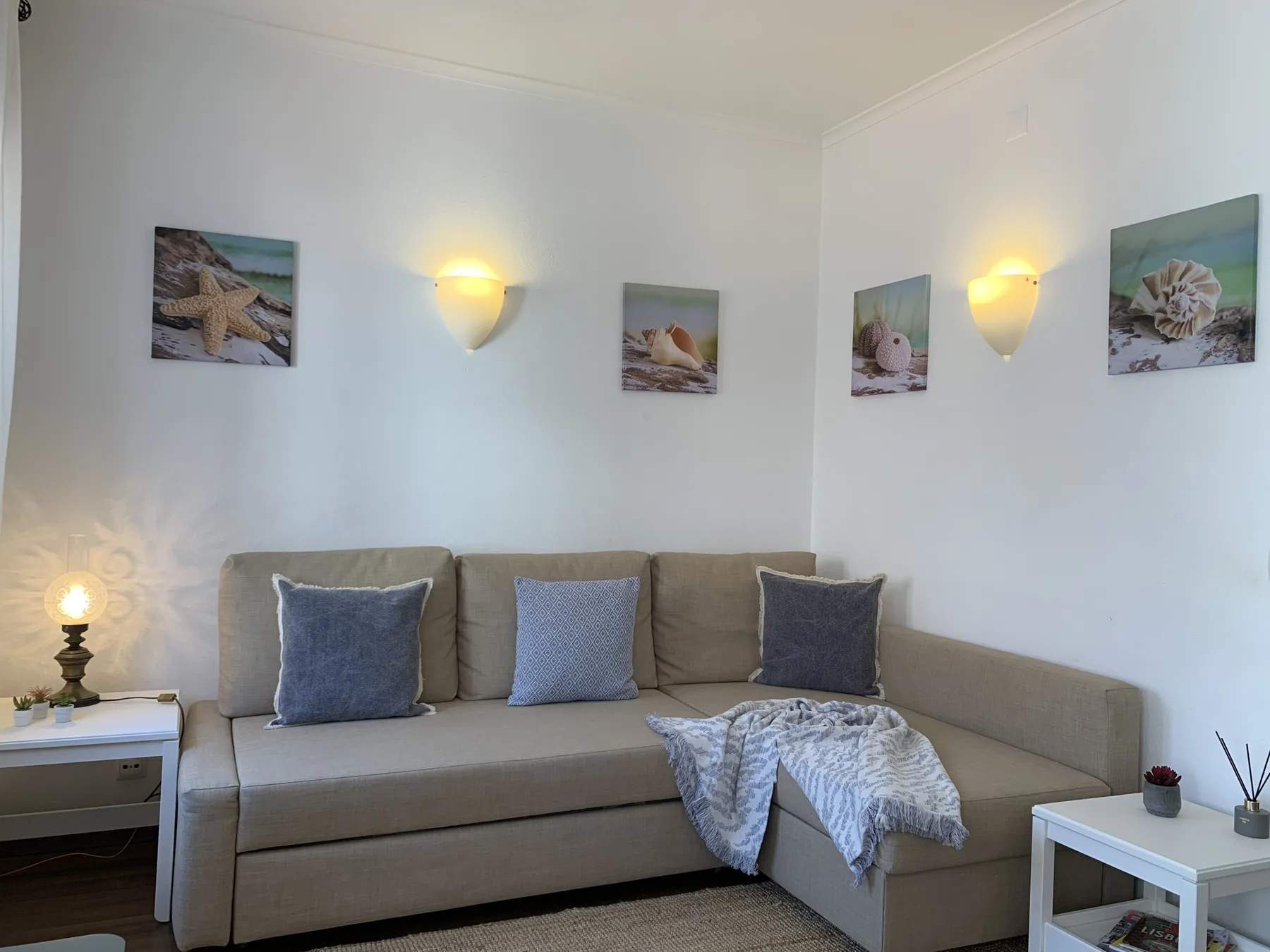 A living room with an L-shaped sofa, wall sconces, and coastal-themed prints.