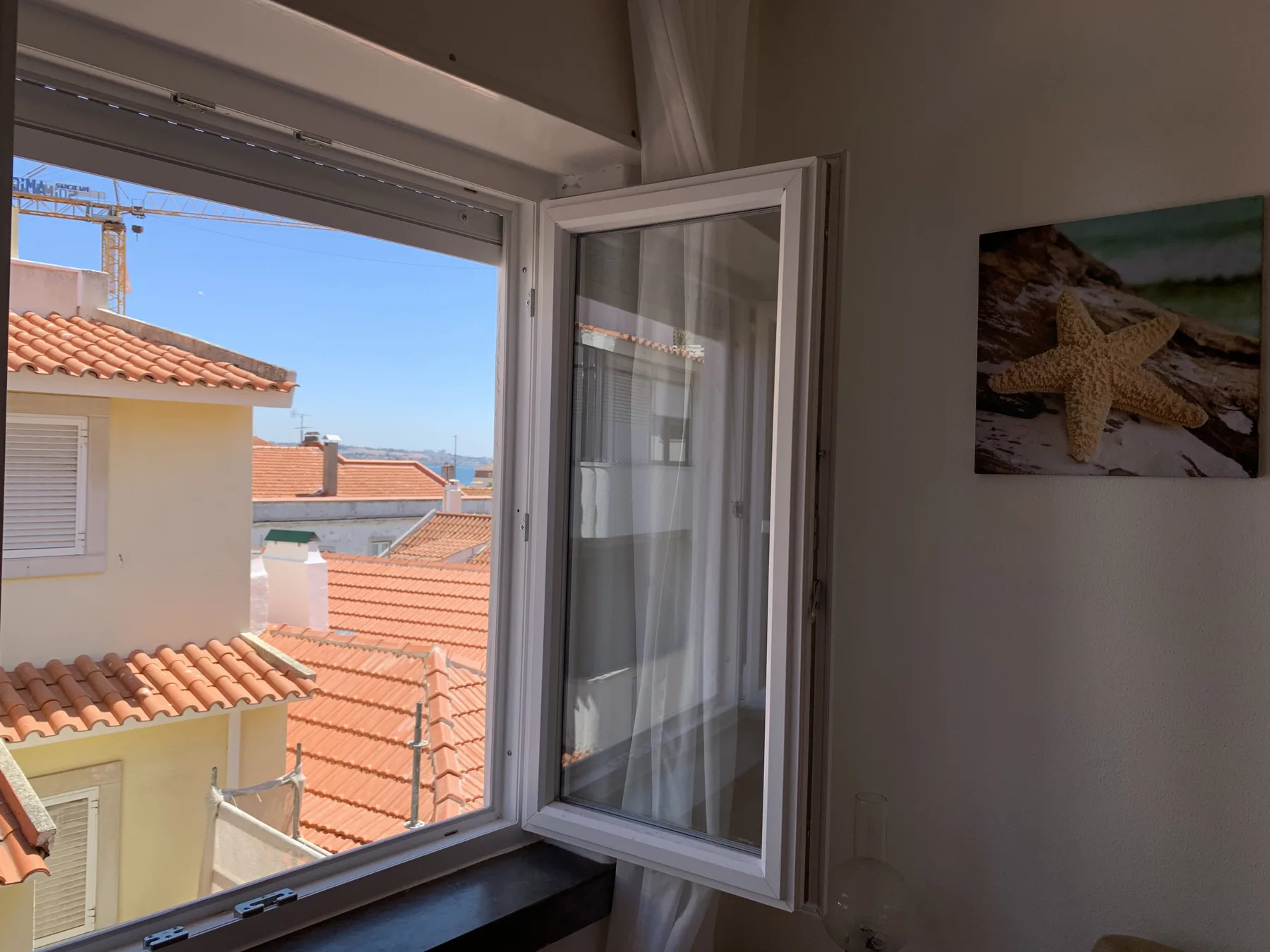 An open window looks out over terracotta rooftops and neighboring buildings.