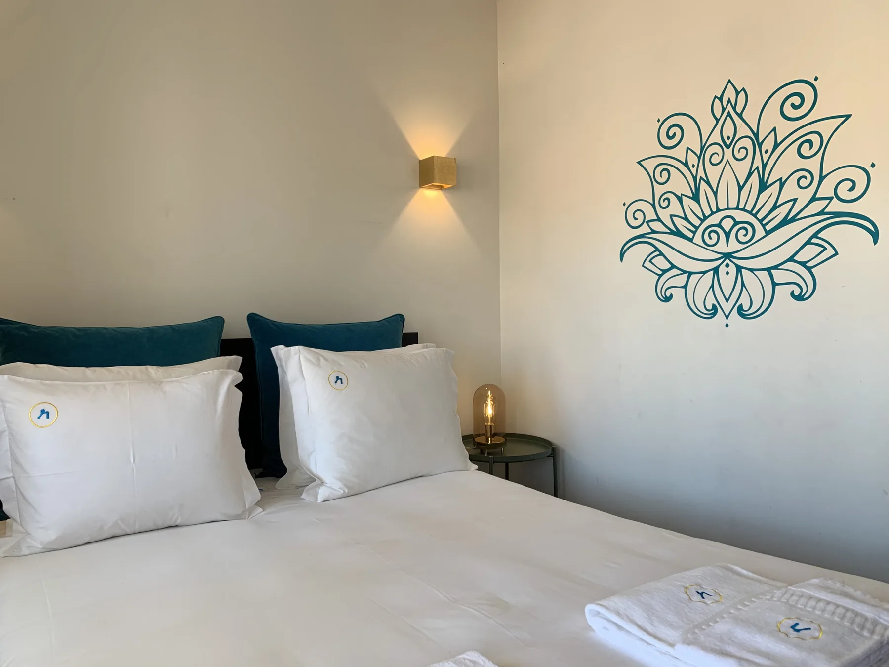 A bedroom with white bedding, teal pillows, and a decorative wall design.