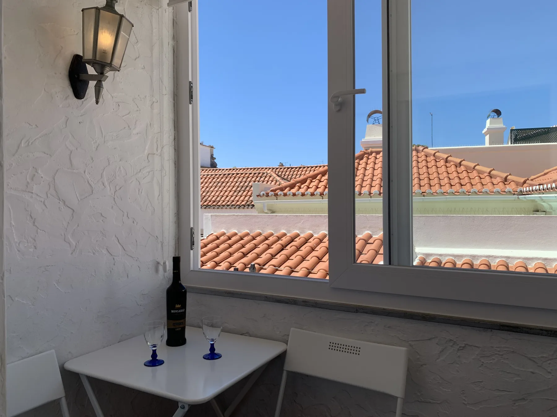 A small dining table sits beside a window overlooking red-tiled rooftops.
