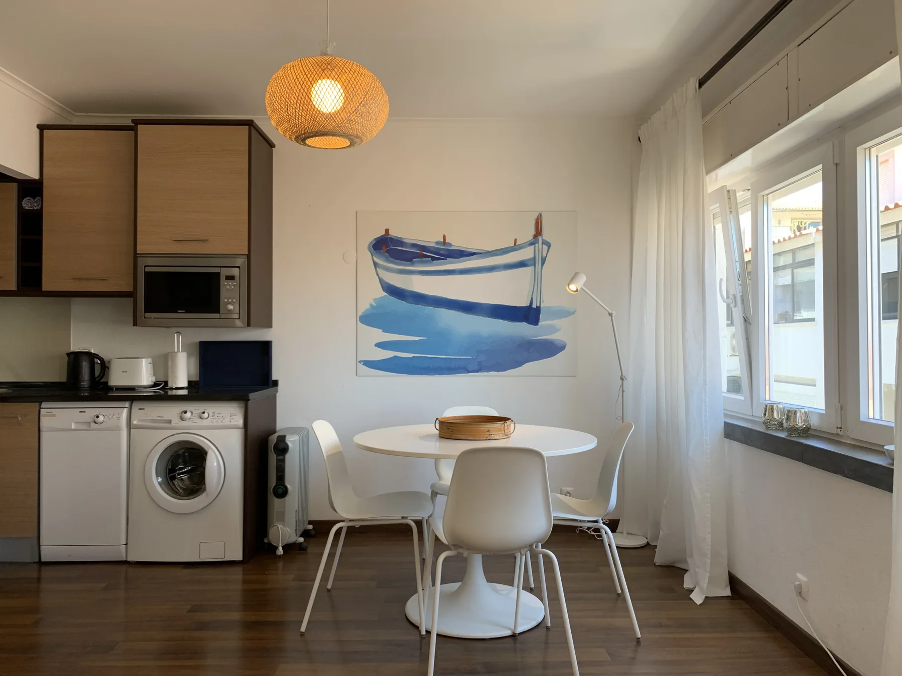 A dining area beside a compact kitchen, with a boat painting on the wall.