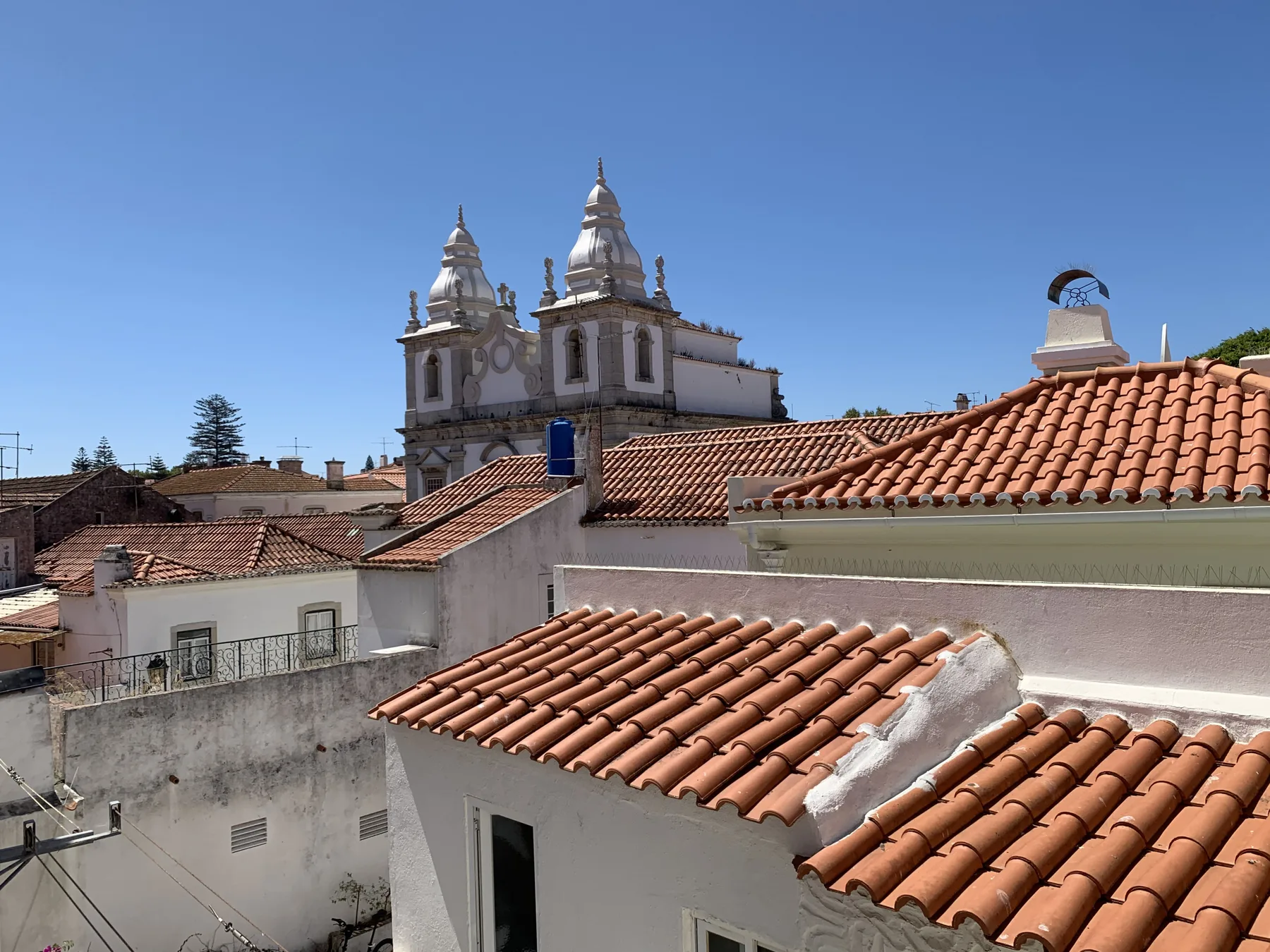 A townscape of white buildings with red tile roofs and a church tower beneath a clear sky.