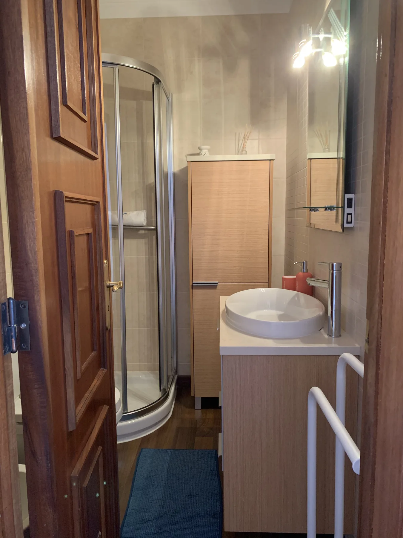 A bathroom with a glass shower, sink, and wood-toned cabinetry.