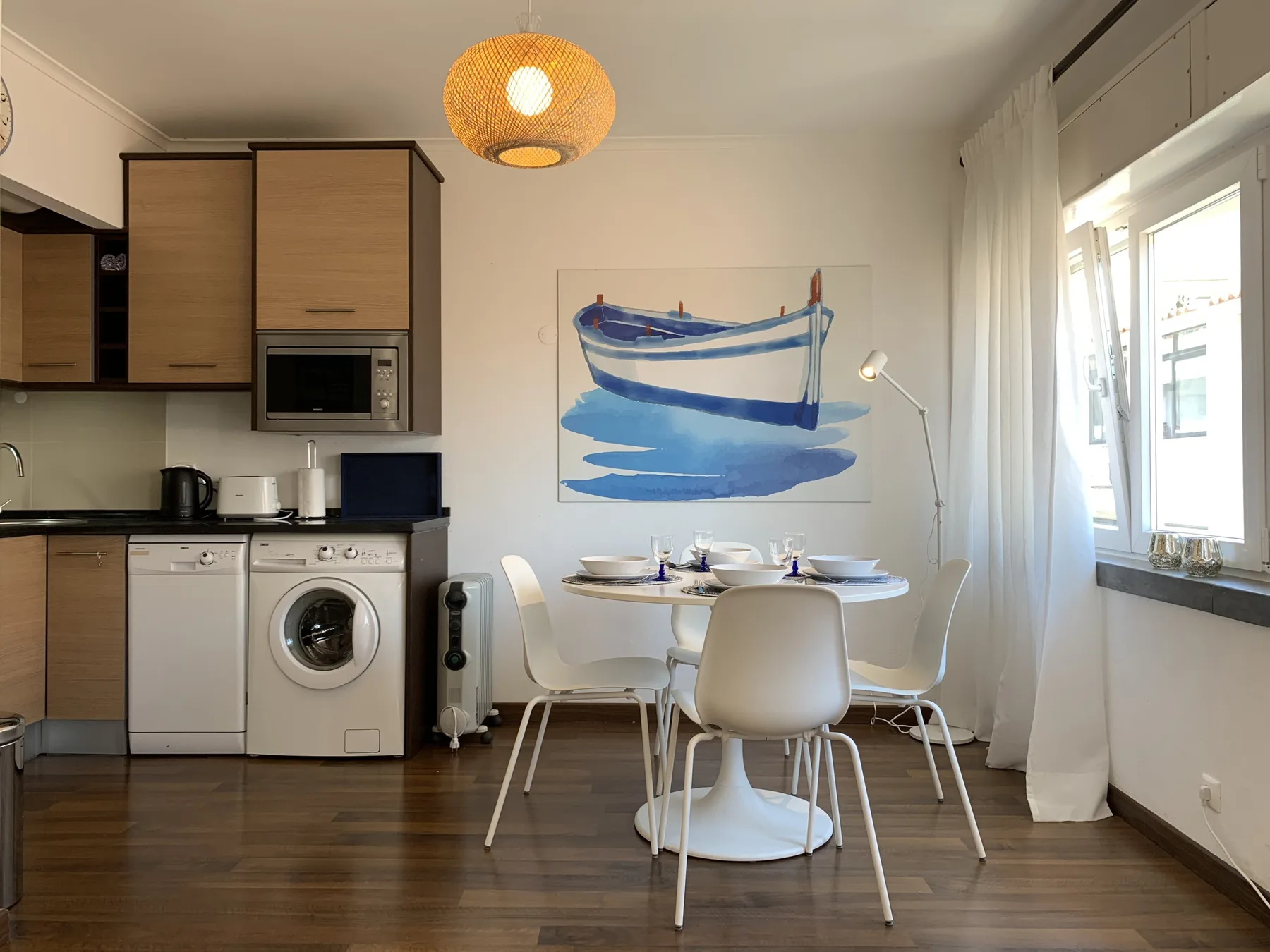 A dining area with a round table and boat painting beside a compact kitchen.