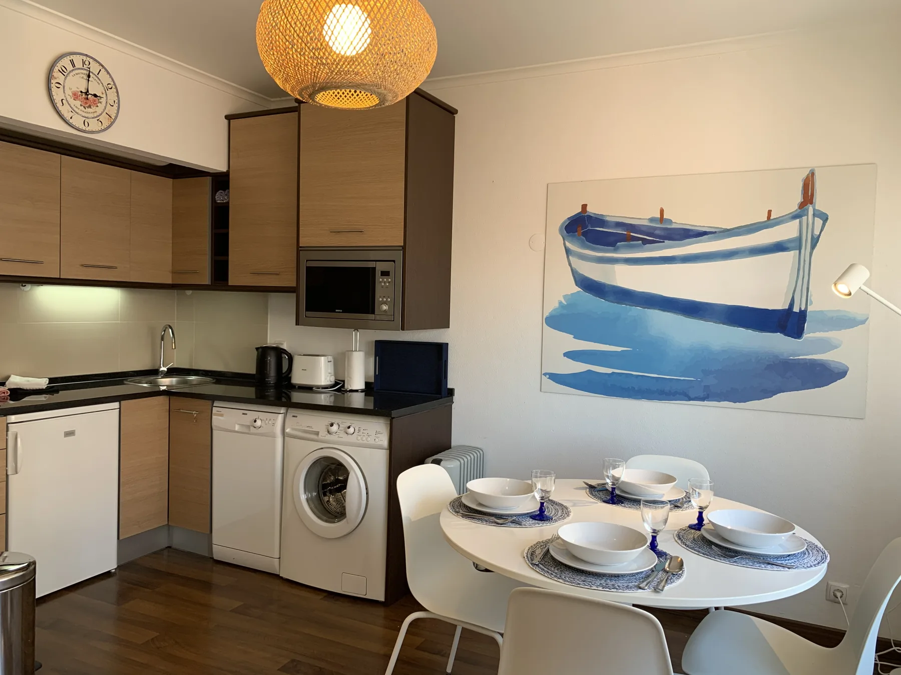 A compact kitchen and dining area with a round table beneath a blue boat painting.