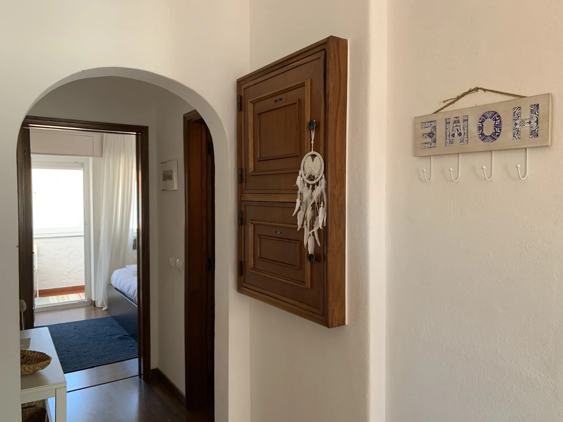 A bright hallway with an arched doorway and a wooden wall cabinet.