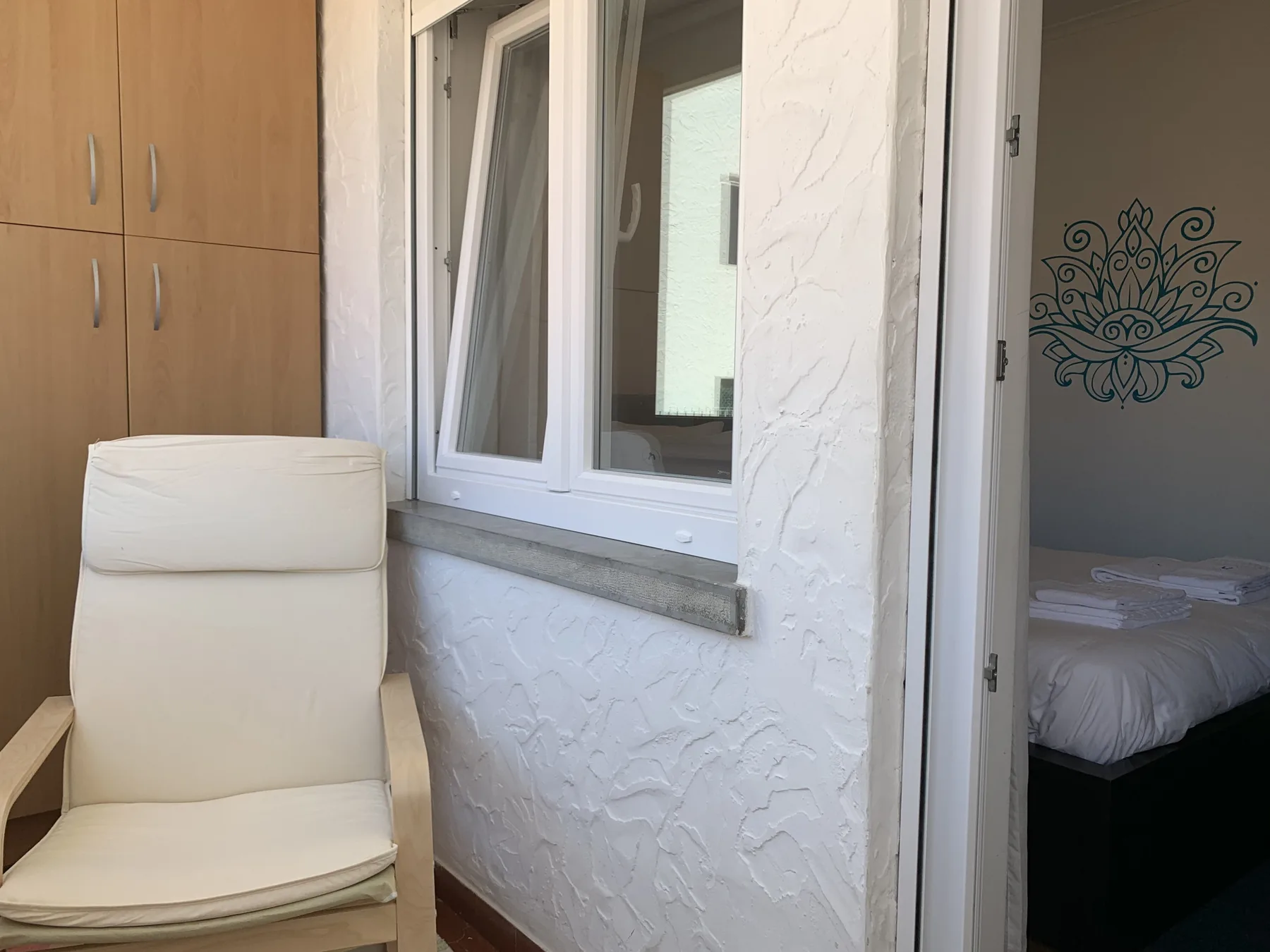 A bedroom is visible through an open doorway beside a window and cushioned seating.