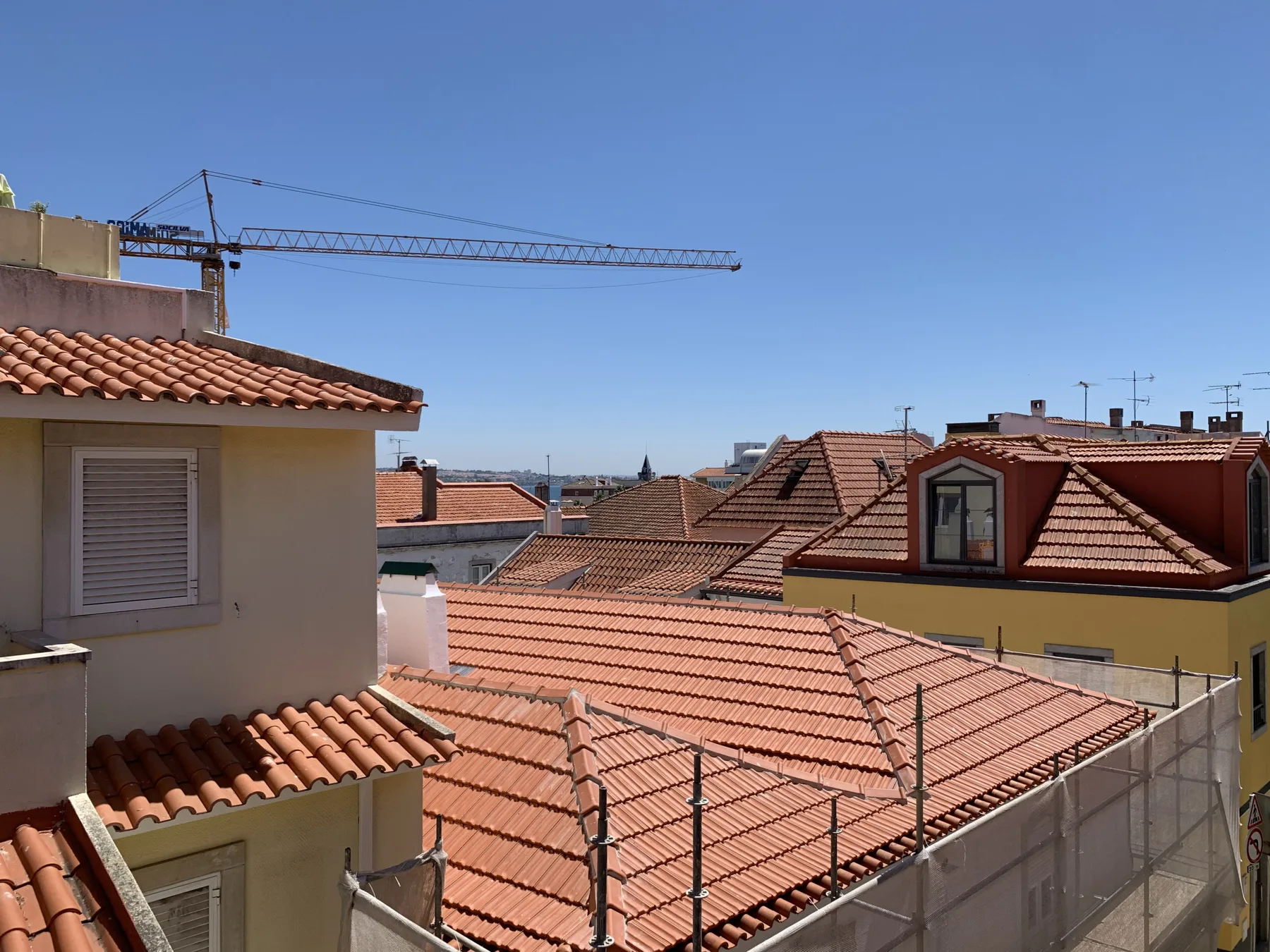 View across terracotta rooftops toward a construction crane under a clear sky.