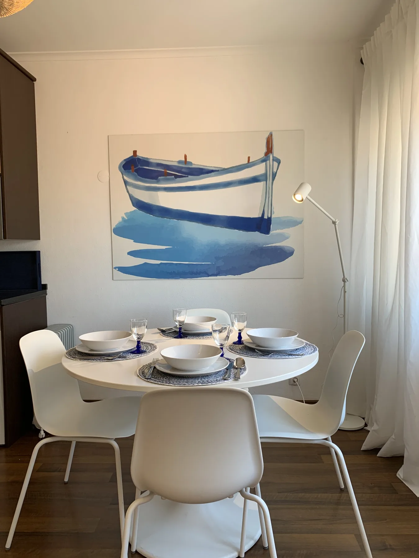 A dining area with a set table beneath a painting of a boat.