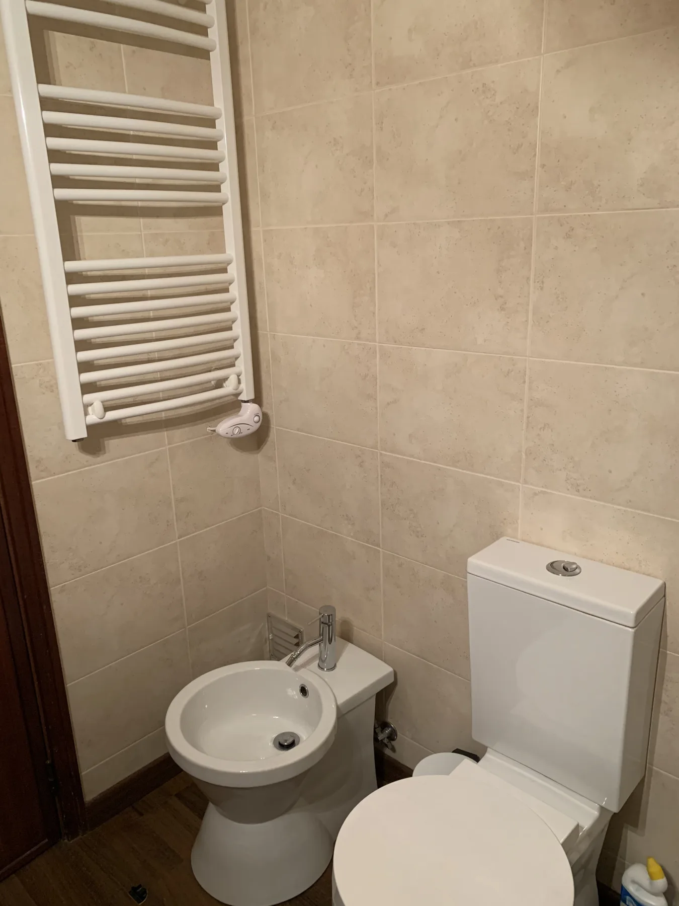 A tiled bathroom with a sink, toilet, and wall-mounted towel warmer.