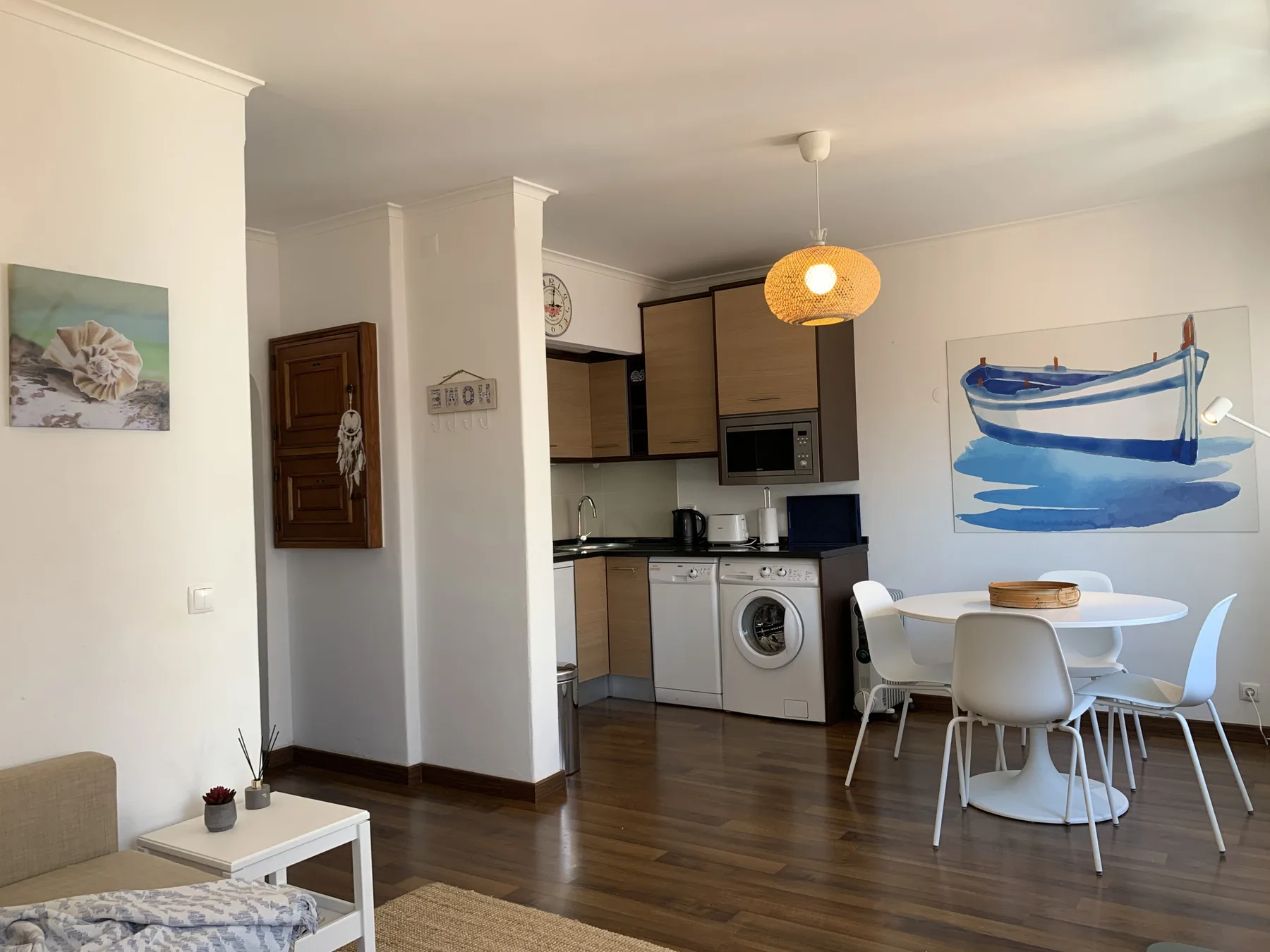 A bright dining and kitchen area with a round table and boat artwork on the wall.
