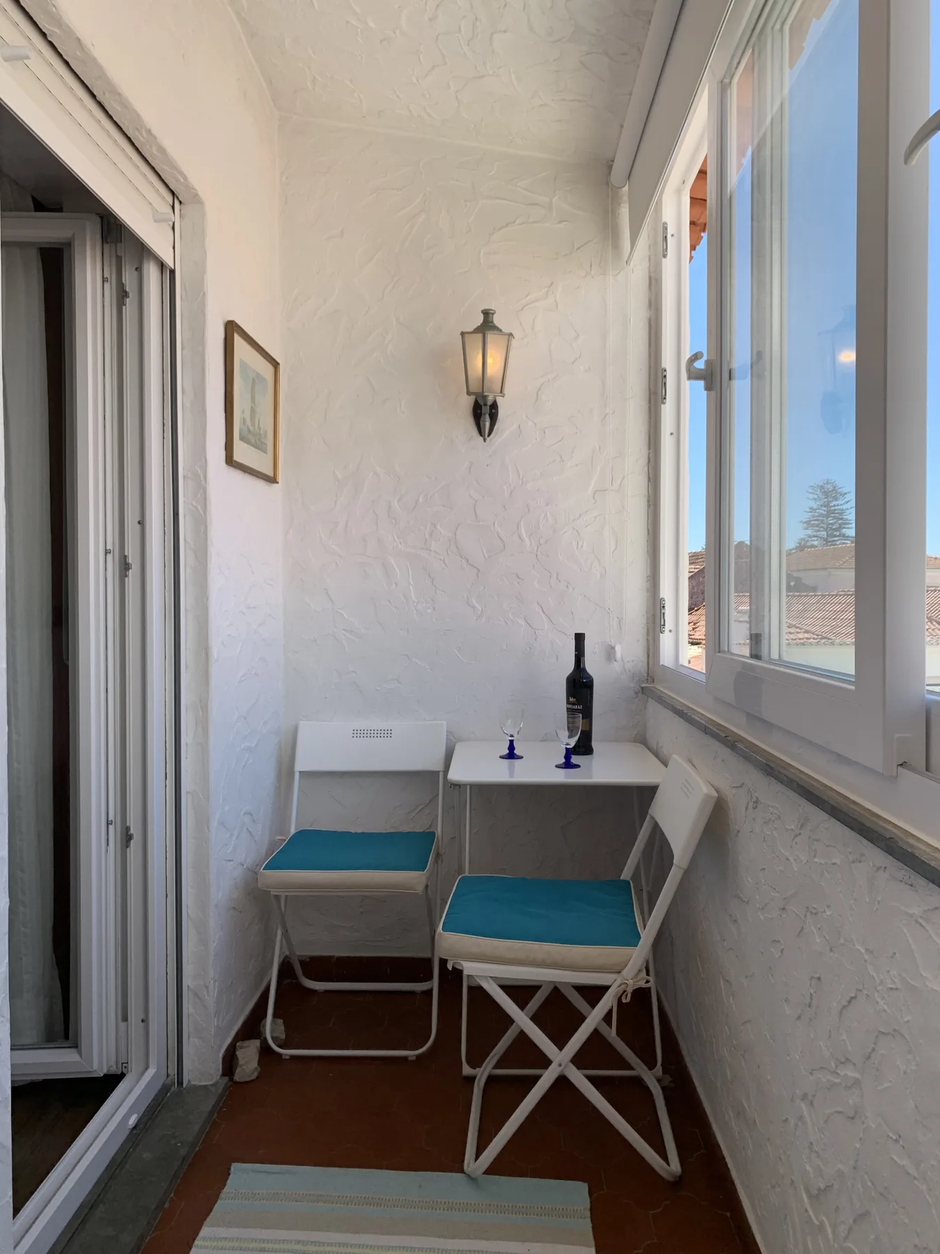 A narrow enclosed balcony has a small table and two seats beside the windows.