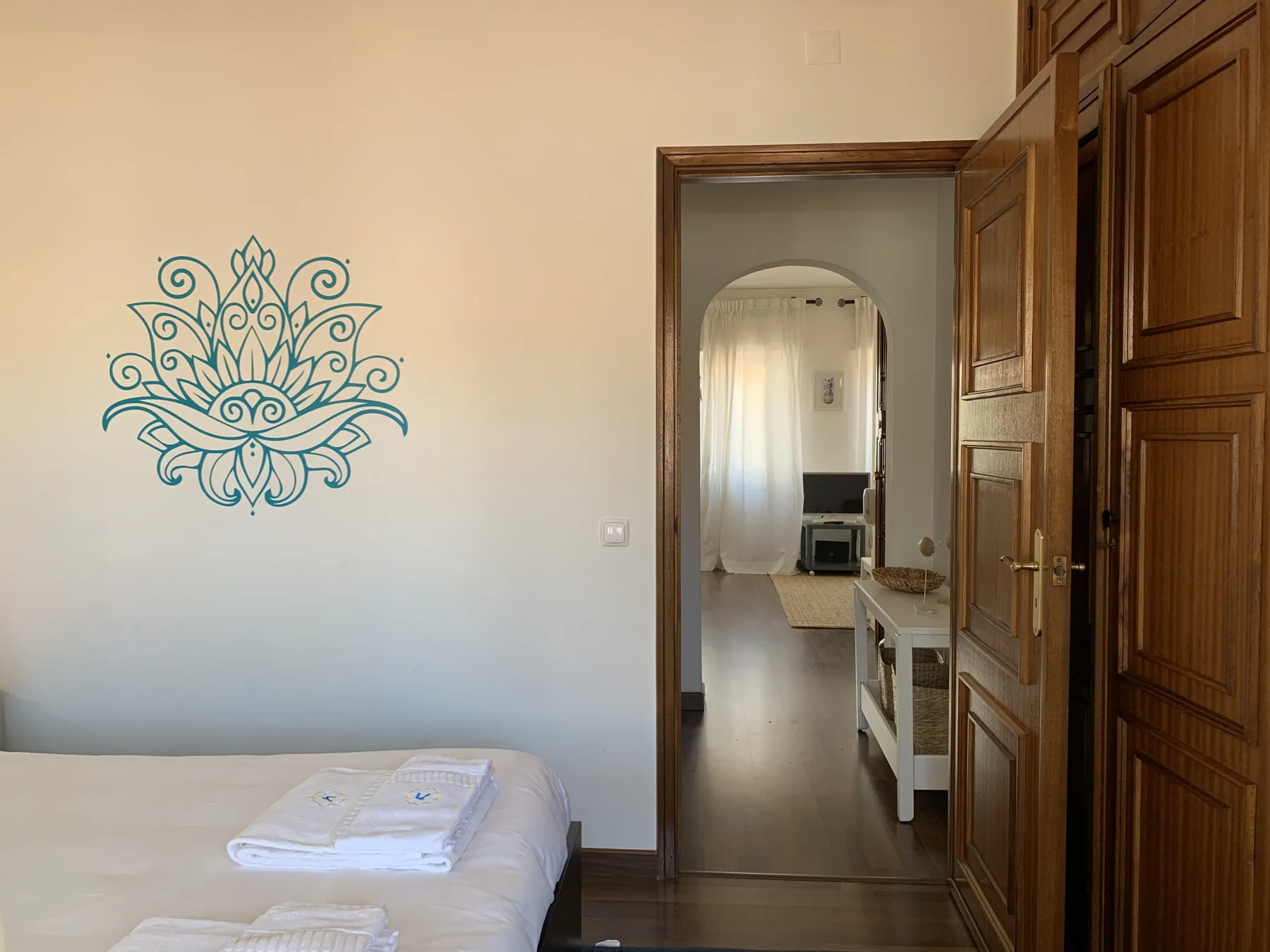 A bedroom with a bed beside an open wooden doorway leading to another room.