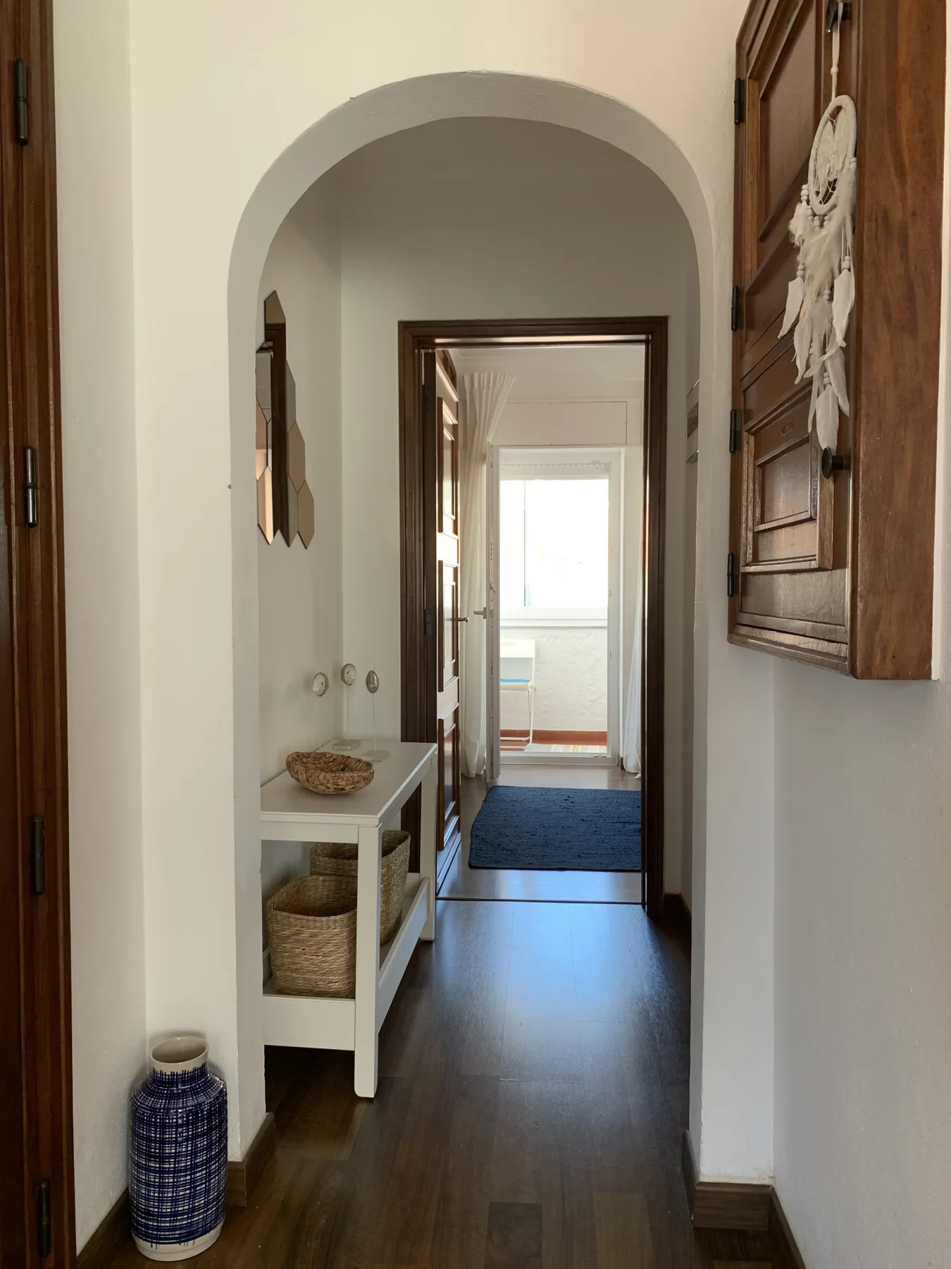 A narrow hallway with an arched opening, a console table, and a blue floor runner.