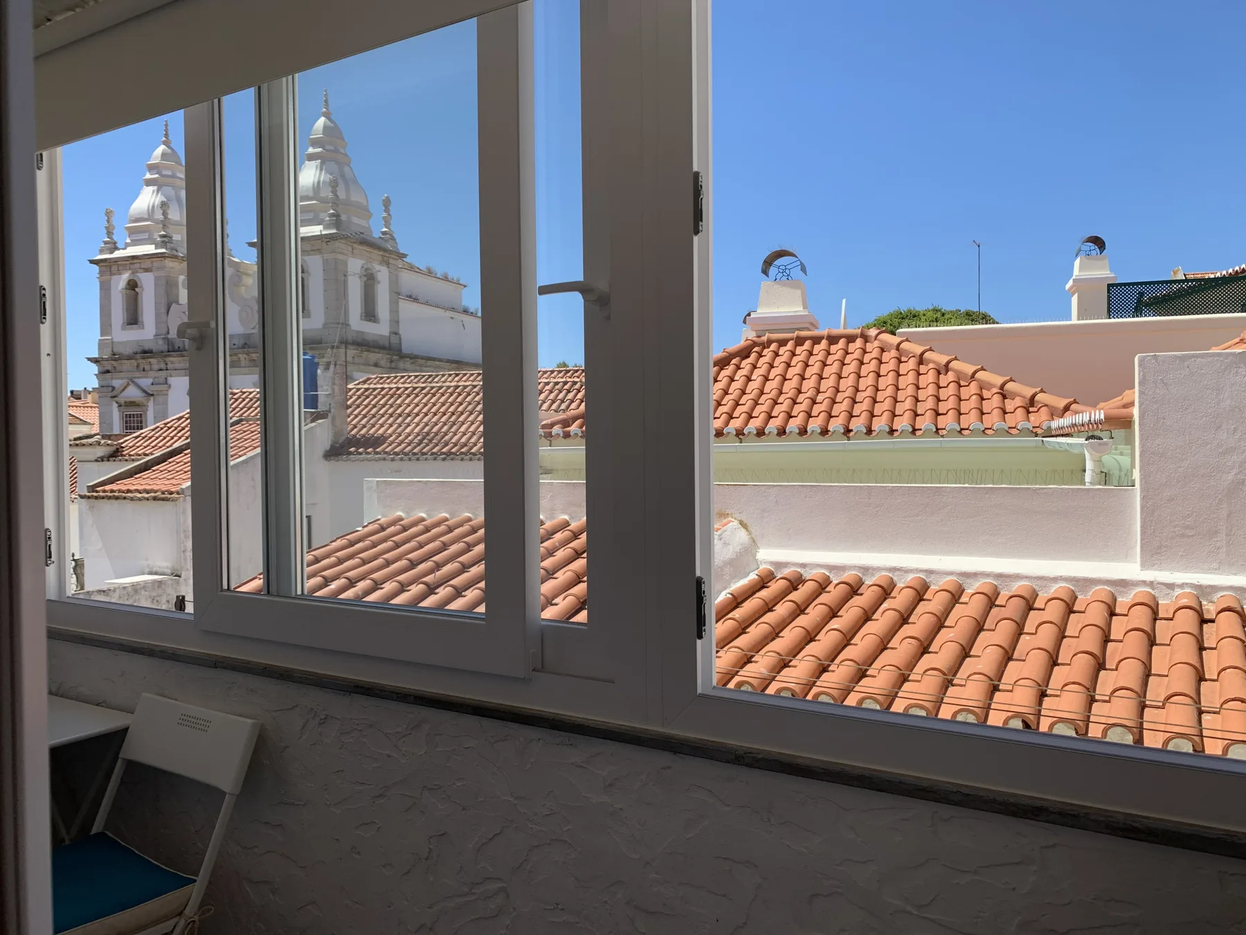 A bright interior room with a large window overlooking tiled rooftops and a church.