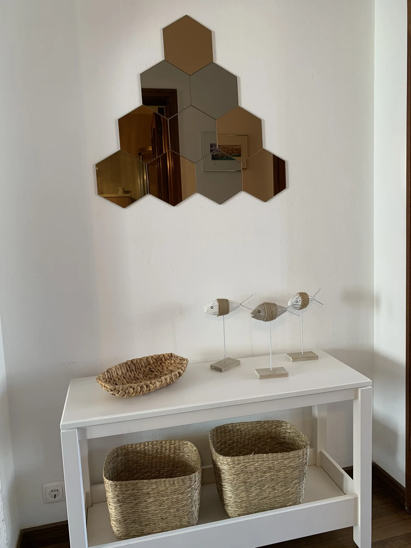 An entryway table with woven baskets beneath a geometric wall mirror.