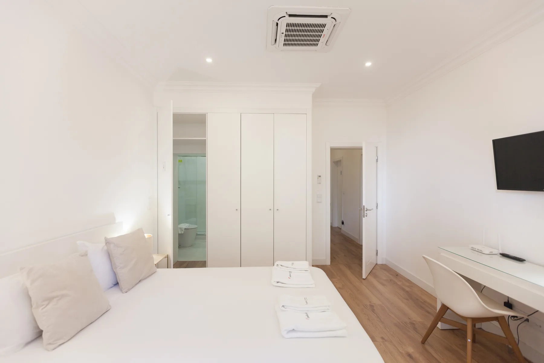 A bright bedroom with a bed, built-in wardrobe, and desk.