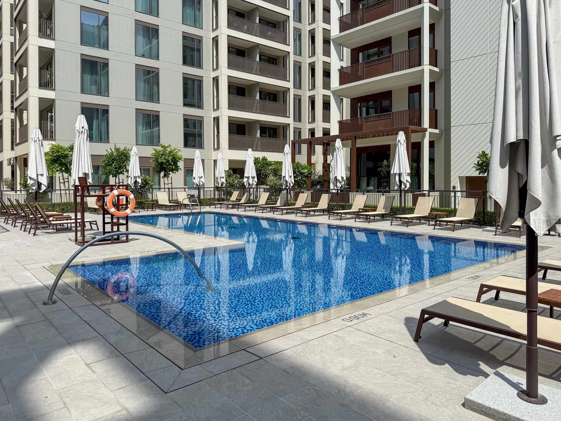 Una piscina al aire libre está rodeada de tumbonas y edificios de apartamentos modernos.