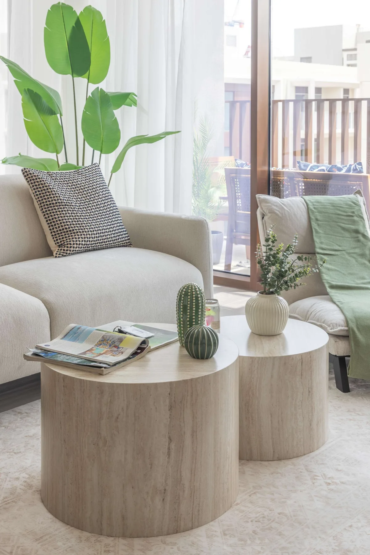 Una sala luminosa con un sofá crema, mesas de centro redondas y plantas frondosas.