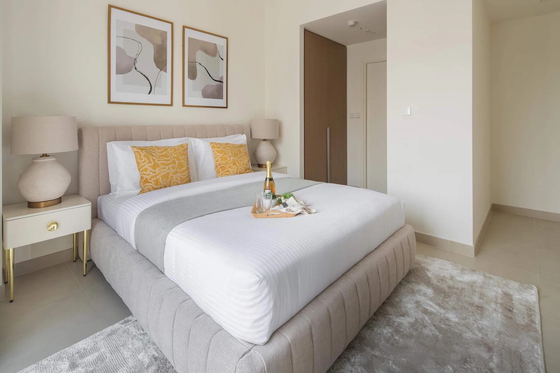 Un dormitorio luminoso con una cama tendida y cuadros enmarcados encima.