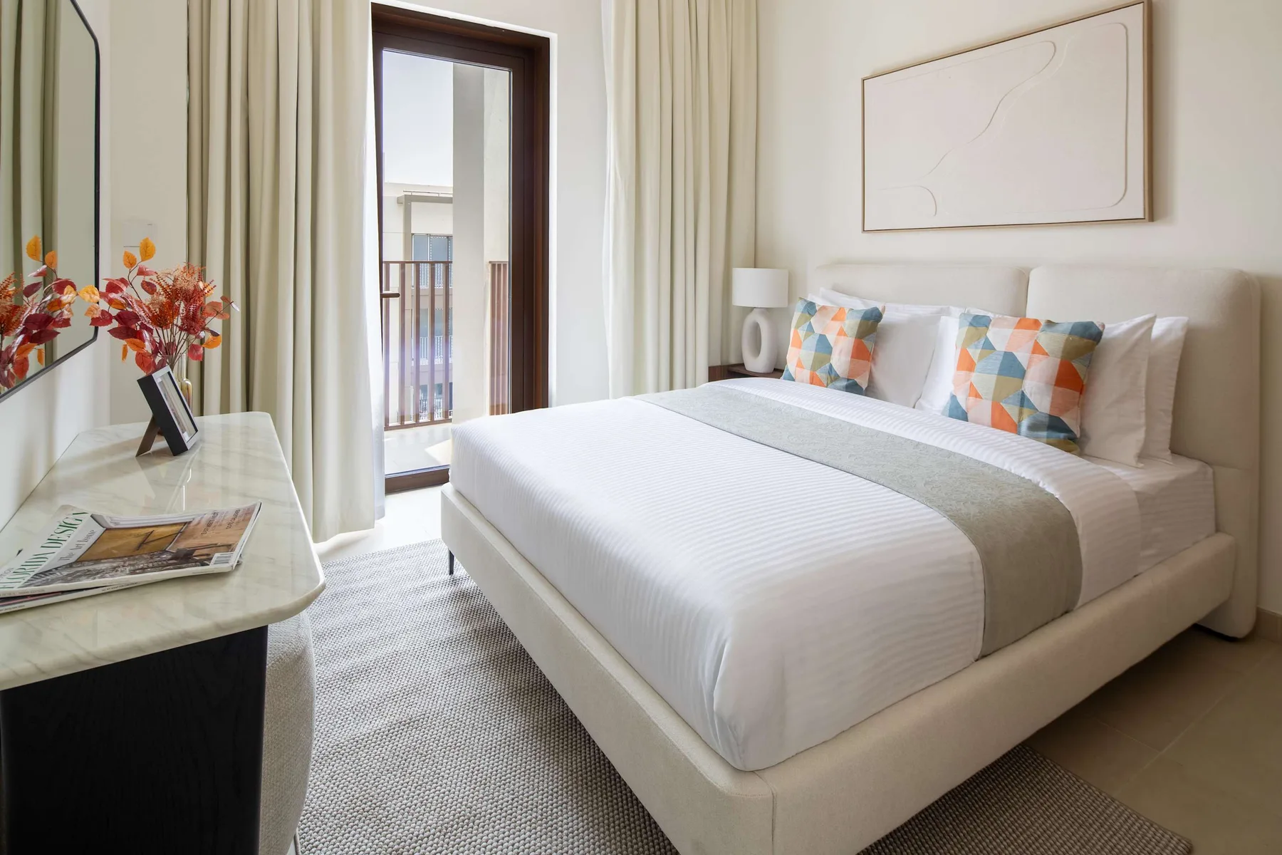 Un dormitorio luminoso con una cama tendida y cojines decorativos de colores.