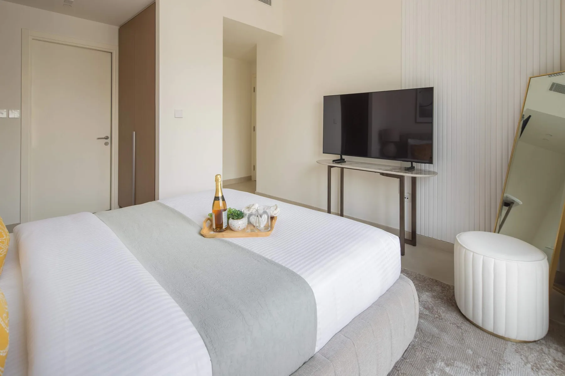 Un dormitorio luminoso con una cama bien tendida y un televisor sobre una mesa.