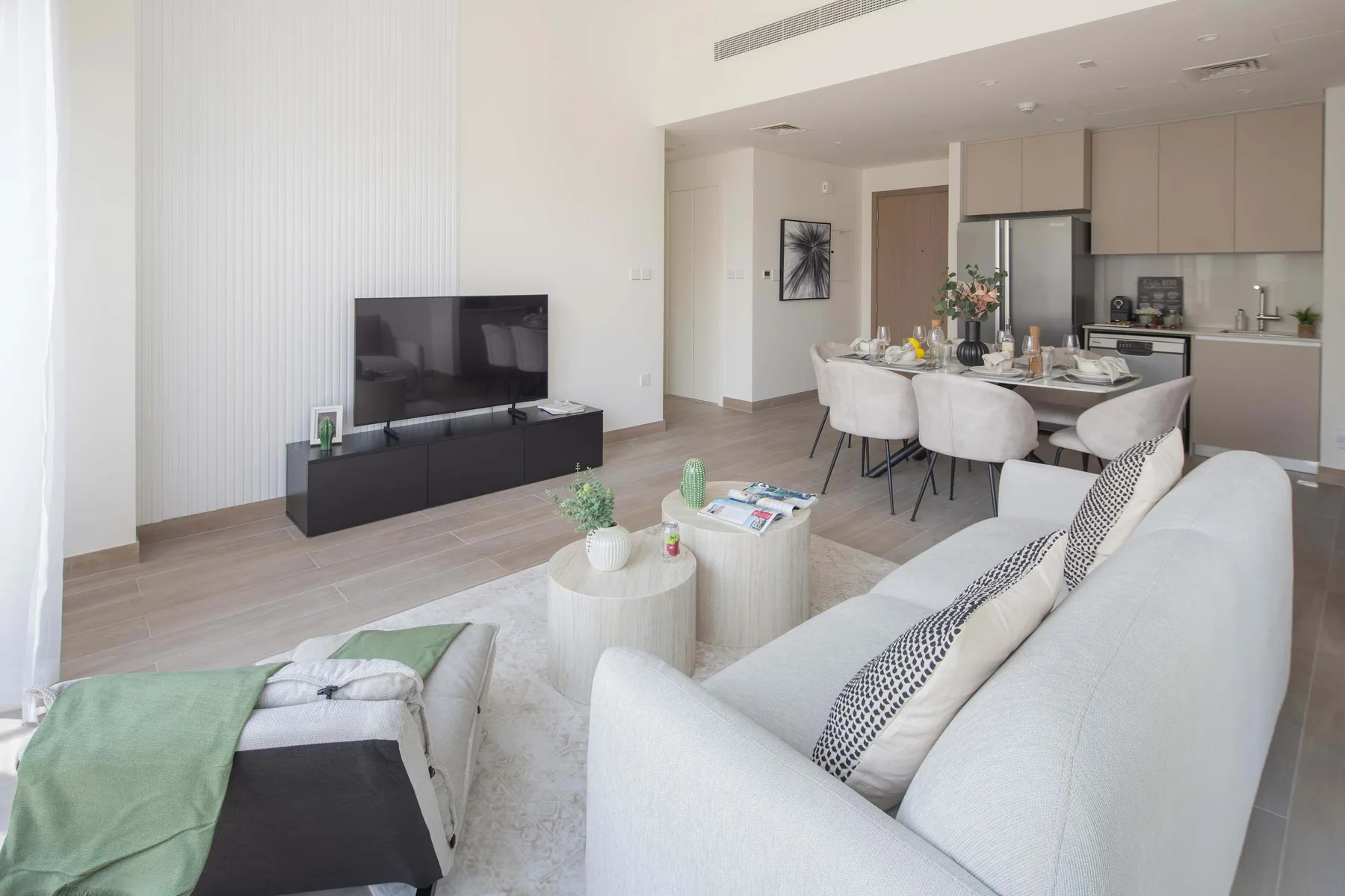 Una luminosa sala de estar y comedor diáfanos, con televisor y asientos claros.