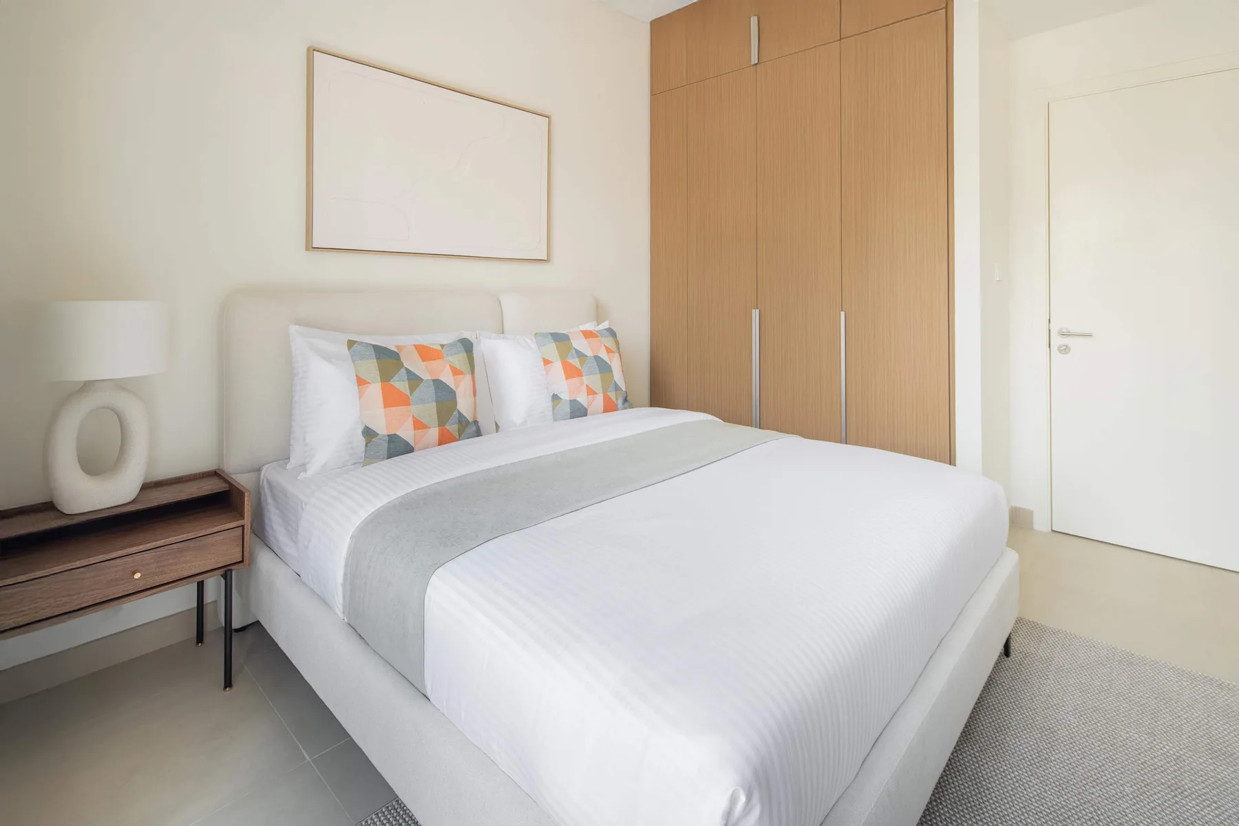 Un dormitorio luminoso con una cama bien hecha y un armario de madera.