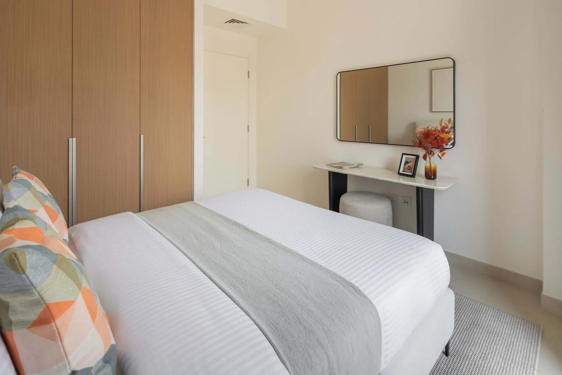 Un dormitorio con una cama tendida y un escritorio bajo un espejo de pared.