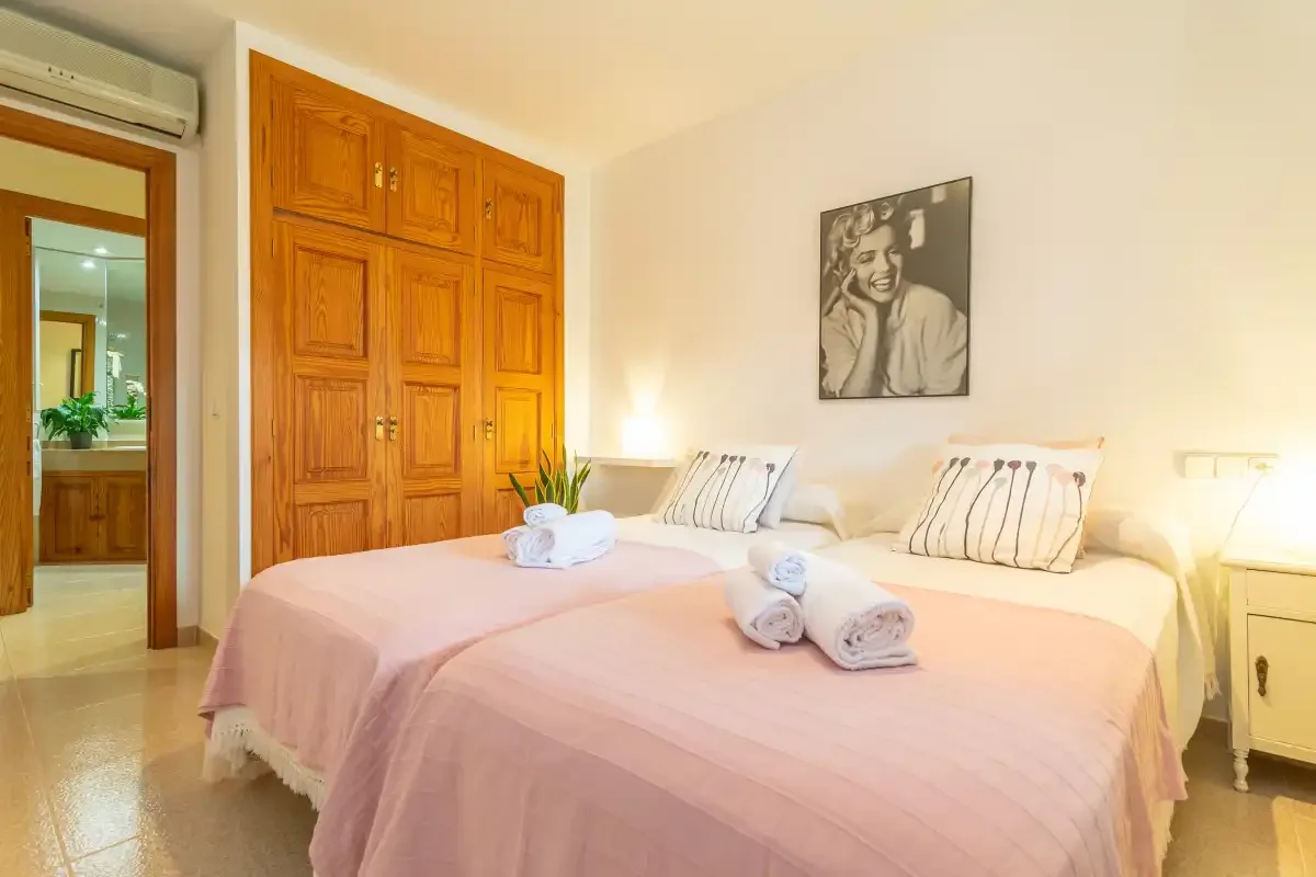 Un dormitorio luminoso con dos camas cubiertas con ropa de cama rosa claro.